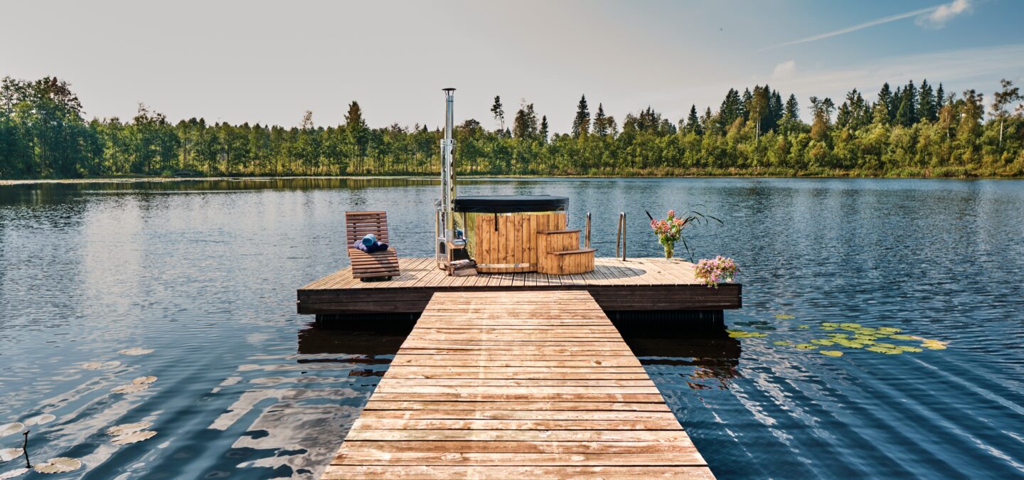 Hot Tub SOPHIA von Feuerbad aus Holz auf einem Steg am See, umgeben von Wald.