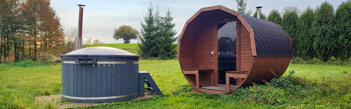 Hot Tub und Fass-Sauna von Feuerbad stehen nebeneinander auf einer Wiese, umgeben von Bäumen